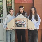 Uczennice z teatrzykiem pod tablicą z nazwą przedszkola.jpg