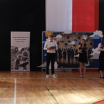 1 Dyrektor szkoły wita zebranych Na scenie uczniowie prowadzący uroczystość.png