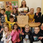 Kinga z VI a z otwartym teatrzykiem kamishibai w otoczeniu dzieci z grupy 5_6 latków Wszyscy machają do biektywu.jpg