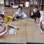 Dzieci siedzą z tabletami przy stoliku - zajęcia - polski dla cudzociemców.jpg