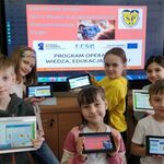 Dzieci z tabletami stoją pod planszą - Tablety z projektu PO WER na zajęciach polski dla cudzociemców004.jpg