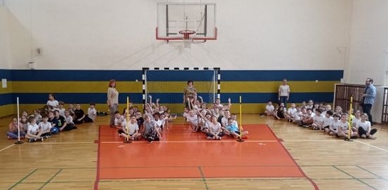 Dzieci w strojach sportowych siedzą w rzędach na sali gimnastycznej.jpg