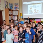 1d Pierwszoklasiści i uczniowie z Aktywu bibliotecznego pod planszą Dzień Głośnego Czytania.jpg