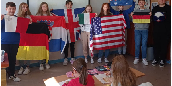 Starsi uczniowie prezentują młodszym flagi różnych krajów.jpg