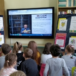 Dzieci patrzą na wielki monitor na którym aktor czyta książkę